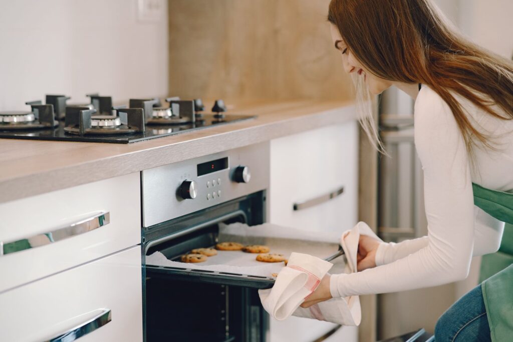Woman taking freshly baked cookies out of the oven at home