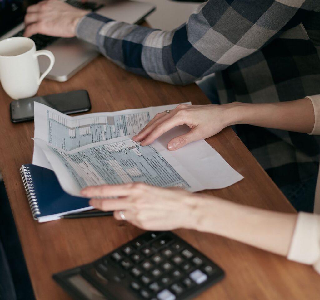 Hands organizing tax forms next to a calculator and laptop