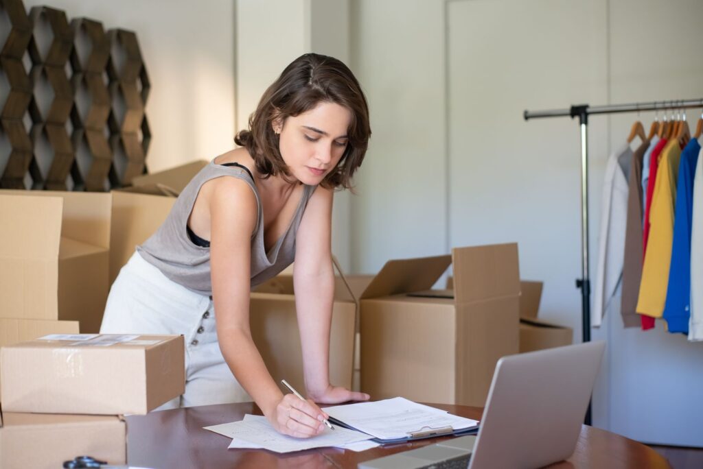 Woman running an online clothing business from her home office with boxes and a laptop