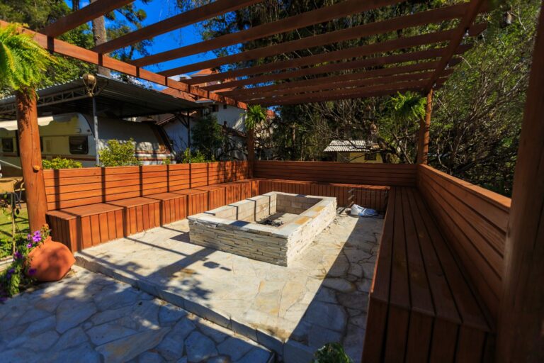 Patio with a stone fire pit and wooden benches under a timber pergola