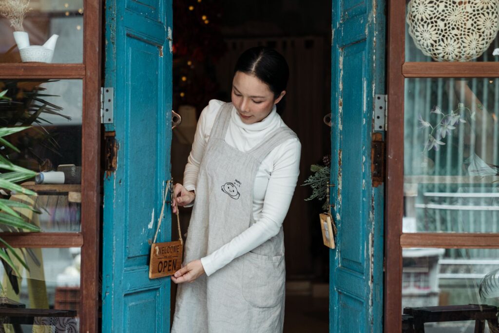 Woman hanging an open sign on the door of her small shop